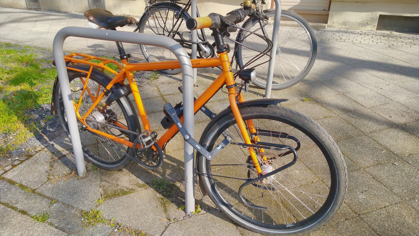 Orangenes Fahrrad steht angeschlossen an einem Fahrradbügel in der Sonne